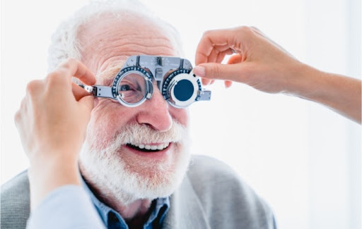 Mature smiling elderly man with white hair being assisted by a female optometrist during an eye exam to check for vision issues.