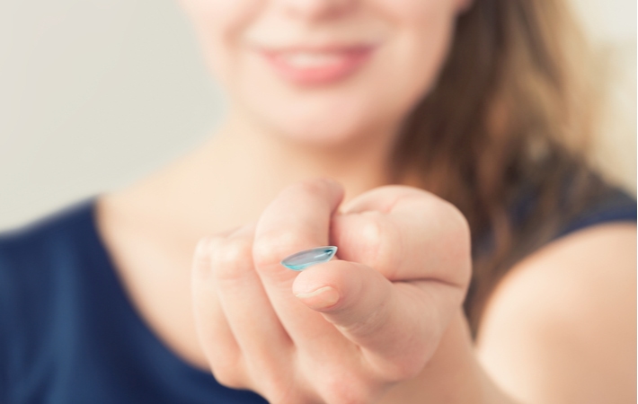 A woman holding out her finger with a contact lens resting on her finger tip