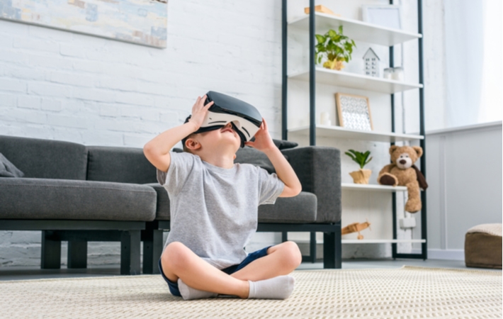 A young boy sitting cross-legged on a carpet in his living room, playing with his VR headset