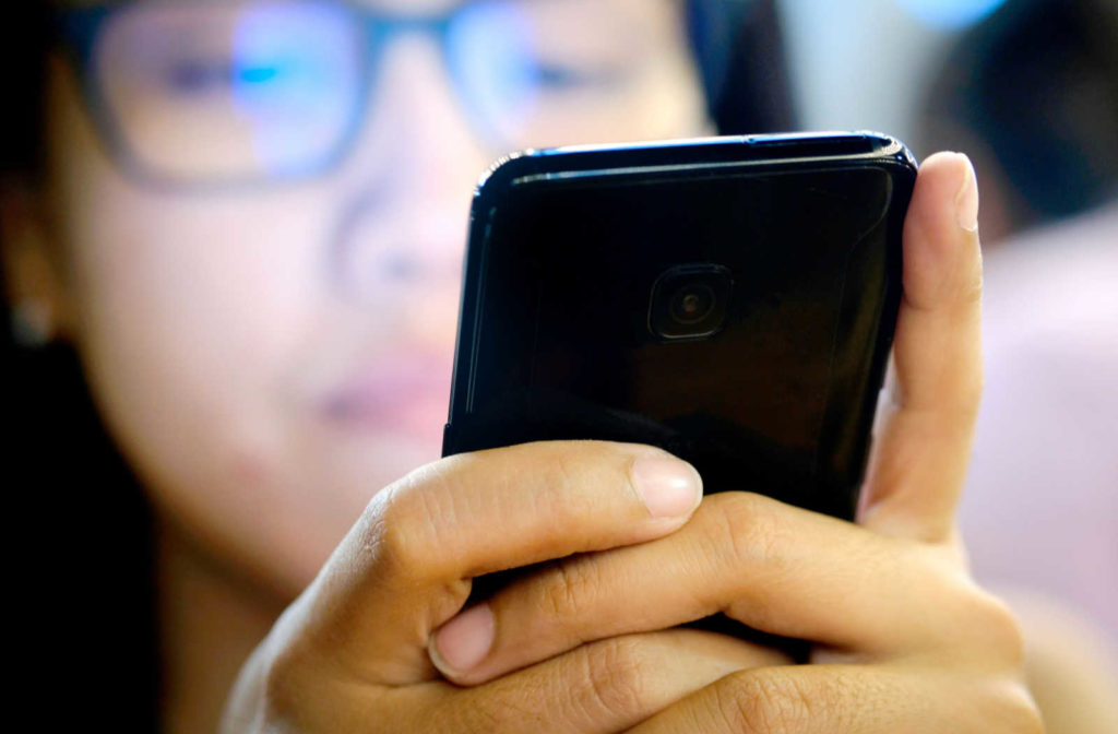 A person staring at their phone screen while wearing blue light glasses to protect their eyes from the symptoms of digital eye strain