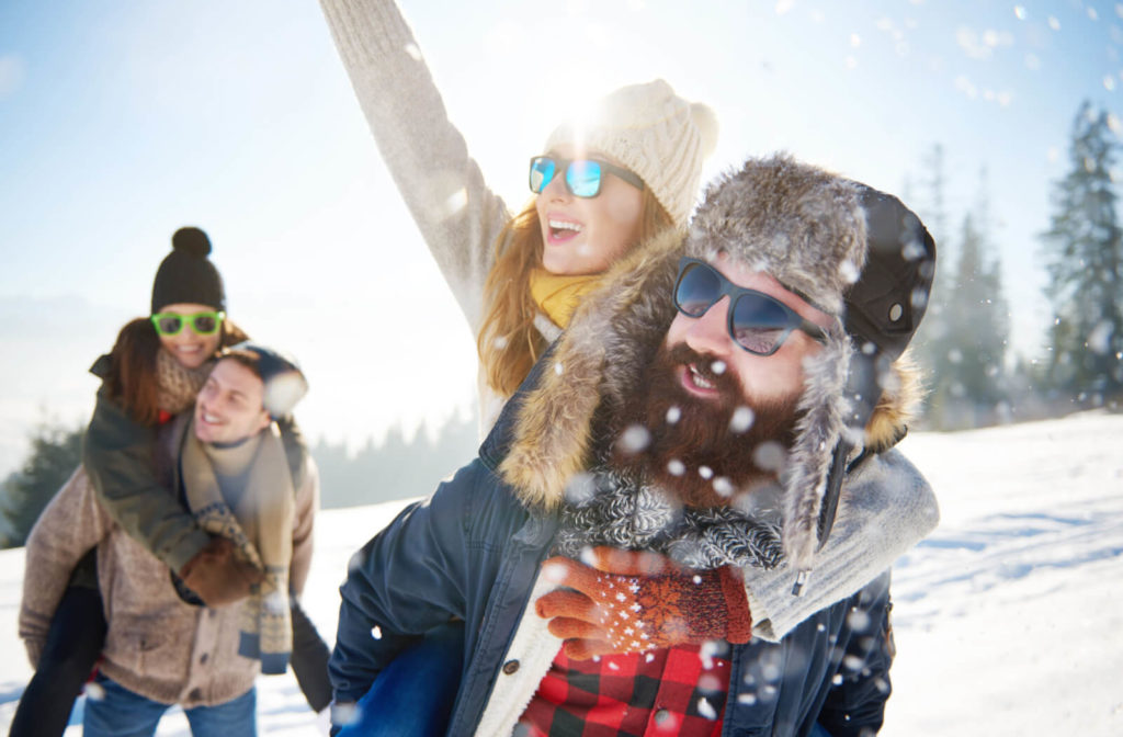 A group of two couples are wearing winter clothes and sunglasses while enjoying  he snow outdoors