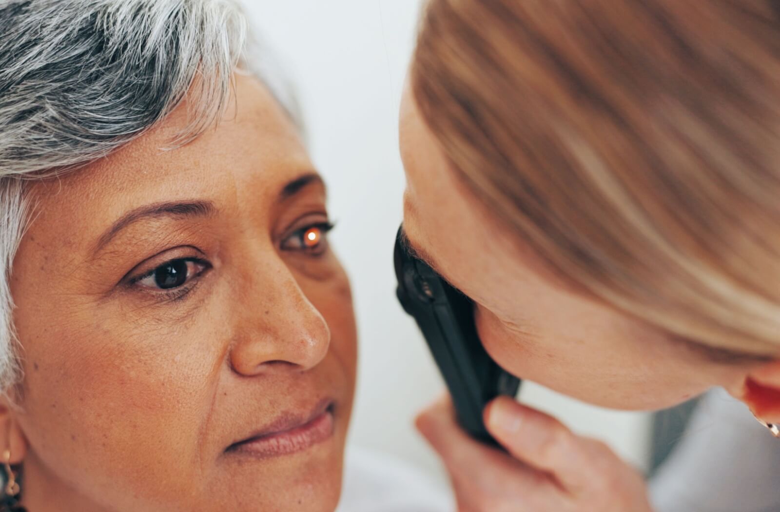 A healthcare professional using an ophthalmoscope to perform a close-up eye examination on a patient, illustrating a routine check for the first signs of glaucoma.